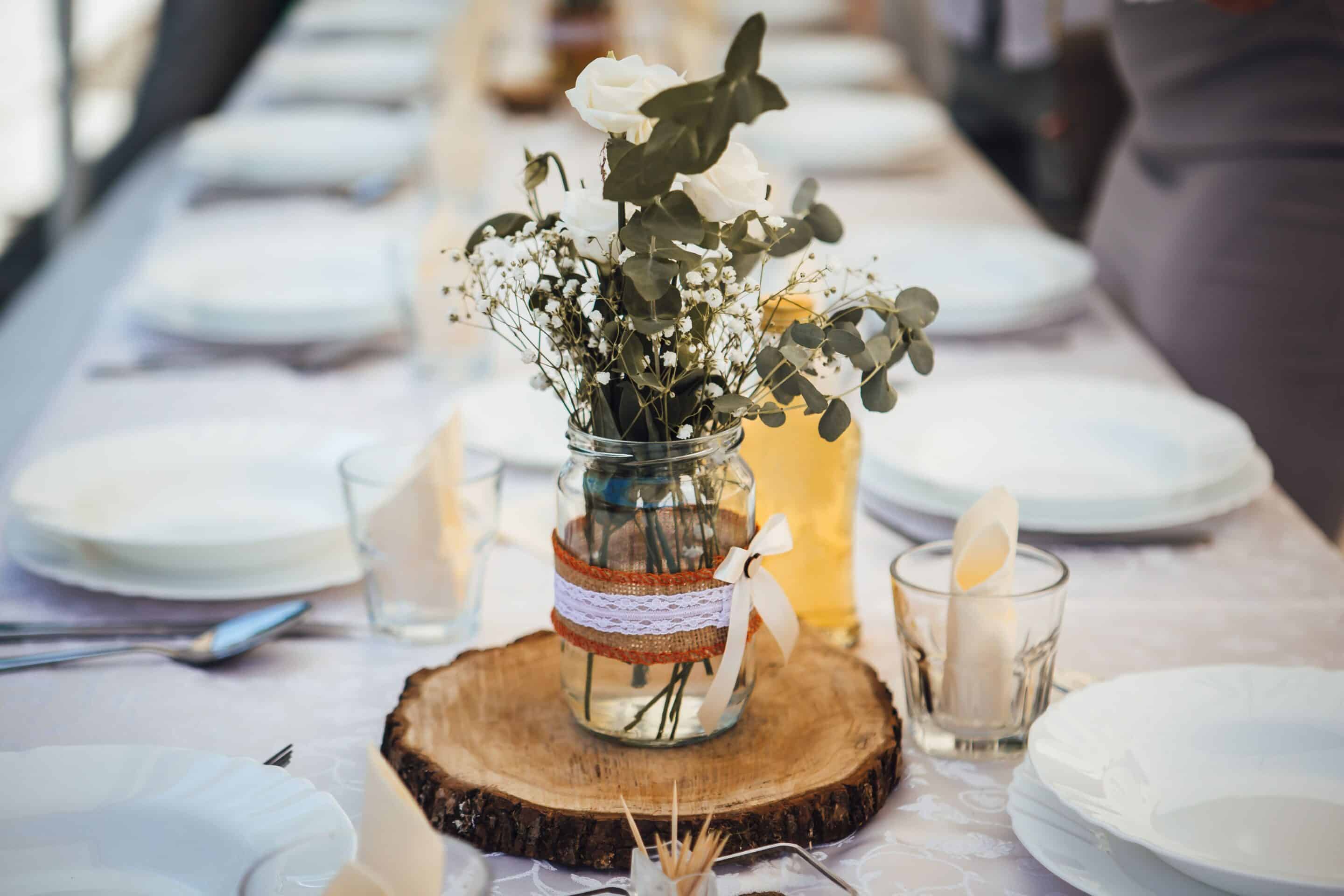 rustic wedding centerpiece of burlap and lace ribbon wrapped around jar of babys breath sitting on a wooden slice