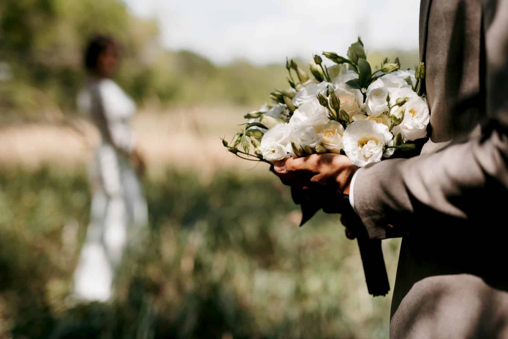 closeup of groom holding bouquet with bride in background